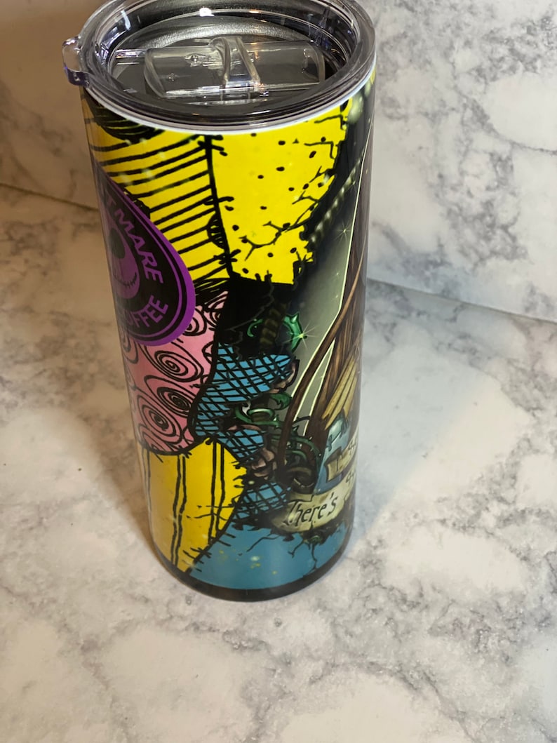 May include: A stainless steel tumbler featuring a colourful graphic of a character from the Nightmare Before Christmas film. The graphic has a patchwork design with yellow, blue, pink and green colours. The text "There's" is visible on the tumbler.