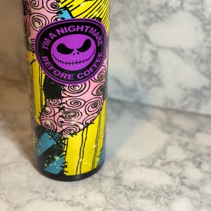 May include: A stainless steel tumbler with a colourful patchwork design featuring the character Jack Skellington from the movie "The Nightmare Before Christmas". The tumbler has a purple circle with the text "I'm a Nightmare Before Coffee".