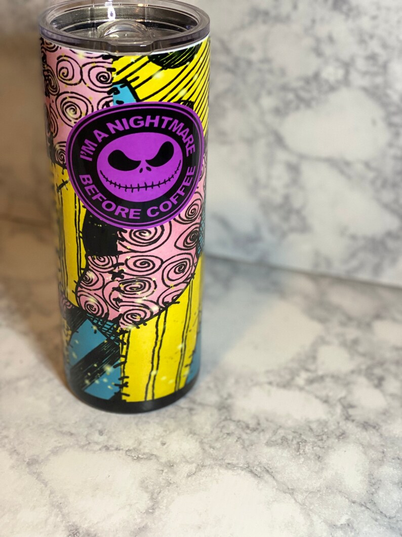 May include: A stainless steel tumbler with a colourful patchwork design featuring the character Jack Skellington from the movie "The Nightmare Before Christmas". The tumbler has a purple circle with the text "I'm a Nightmare Before Coffee".
