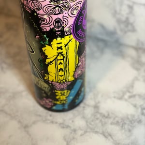 May include: A black and yellow stainless steel tumbler with a colourful graphic design featuring a character from the movie "The Nightmare Before Christmas". The design includes the text "This is Halloween" and "What's This?" The tumbler has a purple lid with a black straw.