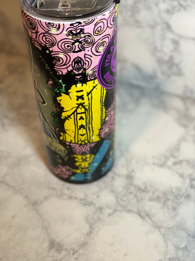 May include: A black and yellow stainless steel tumbler with a colourful graphic design featuring a character from the movie "The Nightmare Before Christmas". The design includes the text "This is Halloween" and "What's This?" The tumbler has a purple lid with a black straw.