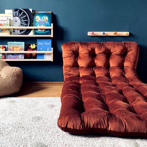 Pode incluir: Um quarto infantil com uma parede azul marinho, uma impressão de leão emoldurada e duas estantes de madeira com livros. Uma cadeira de saco marrom e uma almofada de chão tufada de cor ferrugem estão em um tapete branco felpudo. Um cabide de madeira com pinos coloridos também é visível.
