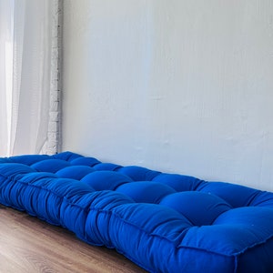 Puede incluir: Un coj&iacute;n de suelo azul capiton&eacute; de forma rectangular. El coj&iacute;n est&aacute; hecho de una tela suave y c&oacute;moda y tiene un dise&ntilde;o simple y moderno.