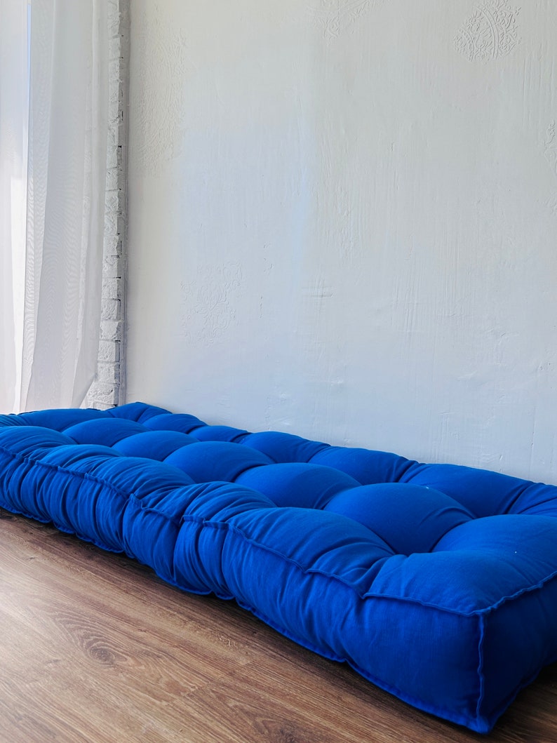 Puede incluir: Un coj&iacute;n de suelo azul capiton&eacute; de forma rectangular. El coj&iacute;n est&aacute; hecho de una tela suave y c&oacute;moda y tiene un dise&ntilde;o simple y moderno.