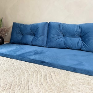 May include: A blue floor cushion with three matching blue back cushions. The cushions are made of a soft, plush fabric and have a tufted design.