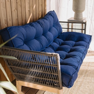 May include: A blue tufted outdoor sofa with a woven gray frame and light wood legs. The sofa has a low profile and is designed for comfort. The cushions are a deep blue color, and the frame is made of a durable material.
