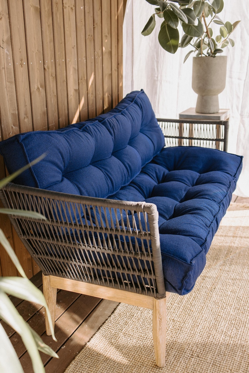 May include: A blue tufted outdoor sofa with a woven gray frame and light wood legs. The sofa has a low profile and is designed for comfort. The cushions are a deep blue color, and the frame is made of a durable material.