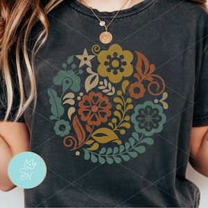 May include: Dark gray t-shirt featuring a circular floral design in shades of orange, green, yellow, and blue. The design includes flowers, leaves, and other botanical elements. The shirt is a casual wear item.
