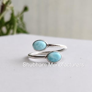 Könnte beinhalten: Ein silberfarbener Ring mit zwei ovalen, hellblauen Edelsteinen. Das Band des Rings umschlingt den Finger, mit einem Stein oben und einem unten. Der Text "Shubham Manufacturers" ist auf der Oberfläche aufgedruckt.