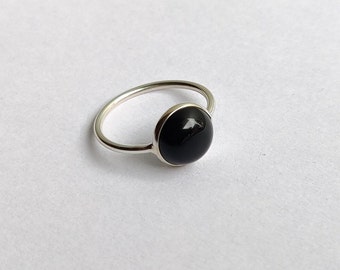 May include: A silver ring with a black gemstone set in a bezel setting.