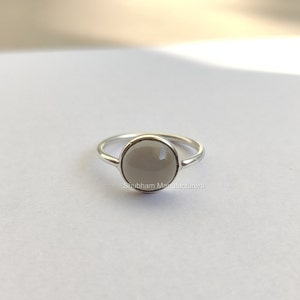 Puede incluir: Un anillo de plata con una piedra preciosa blanca. El anillo está sobre un fondo blanco.