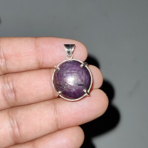 May include: A silver pendant with a large, oval-shaped, purple gemstone set in a silver bezel. The gemstone has a star-like pattern.
