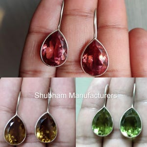 May include: A pair of silver dangle earrings with teardrop-shaped gemstones. The earrings are shown in three different colors: red, green, and brown.