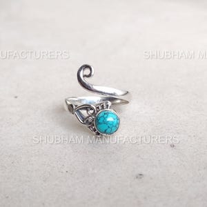 May include: A silver-toned ring with a turquoise stone. The ring features an open design with a decorative swirl and filigree details. The turquoise stone is round and set in a bezel setting.