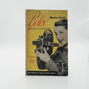 May include: A vintage "Bolex Movie Guide" book with a yellow cover featuring a woman holding a Bolex movie camera. The cover has the Bolex logo and text that reads "with Stereo and Color section". The book is part of "THE MODERN CAMERA GUIDE SERIES".