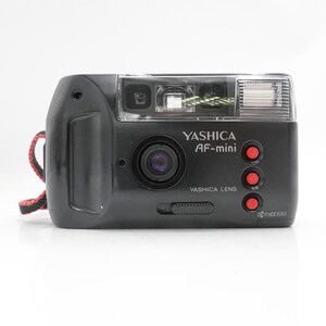 May include: A black Yashica AF-mini point-and-shoot camera with a central lens, a flash unit on the right, and three red circular buttons. The front features the text Yashica AF-mini, Yashica Lens, and Kyocera. A red and black wrist strap is attached.