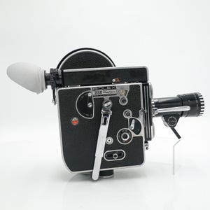 May include: A black Bolex H16 Reflex movie camera with a textured finish, silver metal accents, and a white rubber eyecup. The side panel features various dials, a winding crank, and the text Bolex H16 Reflex Made in Switzerland.
