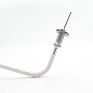 May include: A close-up of a metal and white tool with a gear-like component and a thin, pointed tip. The tool has a curved white handle and is set against a white background.