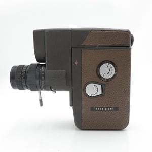 May include: A vintage Arco Eight film camera. The camera has a brown textured body with a black lens and viewfinder. The lens has measurement markings. The camera has two silver dials and the text "ARCO EIGHT".