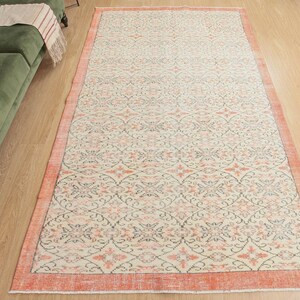May include: A vintage-style rug with a cream background and a repeating pattern of pink and grey floral designs. The rug has a peach-coloured border.