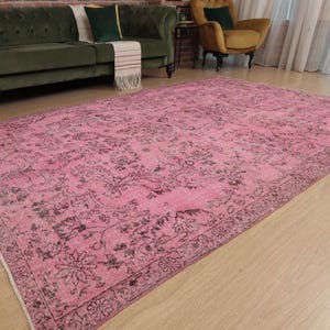 May include: A large rectangular area rug featuring a vibrant pink base color with intricate, dark charcoal-colored floral and vine patterns throughout the center and a detailed decorative border framing the entire piece.