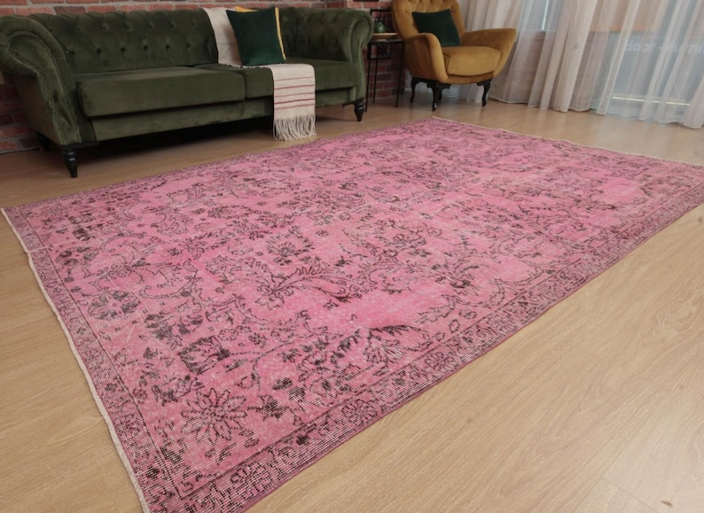May include: A large rectangular area rug featuring a vibrant pink base color with intricate, dark charcoal-colored floral and vine patterns throughout the center and a detailed decorative border framing the entire piece.