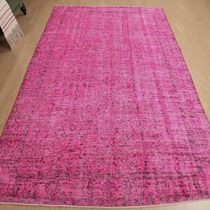 May include: A large, rectangular rug in a vibrant pink colour. The rug has a distressed, vintage-inspired design with darker accents, creating a textured appearance. The rug is placed on a light-coloured wooden floor.