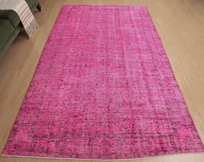 May include: A large, rectangular rug in a vibrant pink colour. The rug has a distressed, vintage-inspired design with darker accents, creating a textured appearance. The rug is placed on a light-coloured wooden floor.