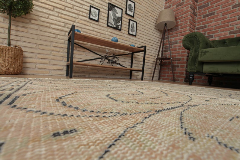 May include: A beige rug with a black and white geometric pattern. The rug is laid out on a wooden floor in front of a brick wall.