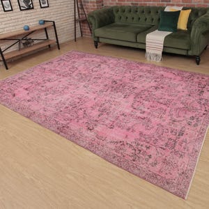May include: A large rectangular area rug featuring a vibrant pink base color with intricate, faded dark gray floral and botanical patterns throughout. The rug has a detailed border design and a low-pile texture, covering a significant portion of the floor.