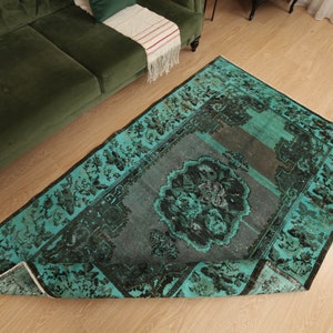 May include: A teal and black vintage rug with a floral pattern. The rug is folded in half and is lying on a wooden floor.