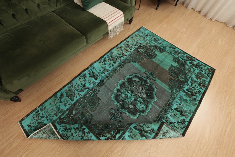 May include: A teal and black vintage rug with a floral pattern. The rug is folded in half and is lying on a wooden floor.