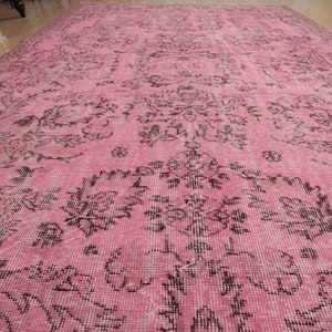 May include: A large rectangular area rug featuring a vibrant pink base color with a repeating dark brown floral and botanical pattern. The design consists of intricate, symmetrical motifs spread across the entire surface of the woven textile.