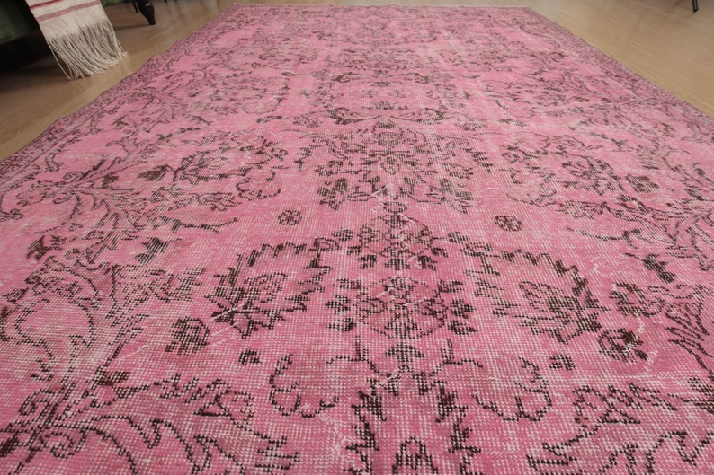 May include: A large rectangular area rug featuring a vibrant pink base color with a repeating dark brown floral and botanical pattern. The design consists of intricate, symmetrical motifs spread across the entire surface of the woven textile.