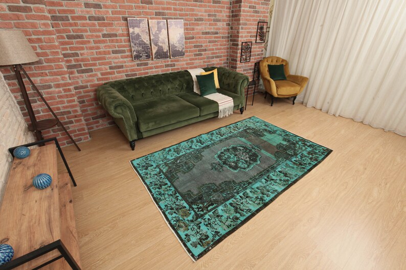 May include: A teal and black vintage rug with a floral pattern. The rug is laid out on a wooden floor in a living room setting.