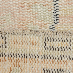 May include: Close-up of a woven rug with a cream, beige, and brown color scheme. The rug has a textured surface and a fringe border.