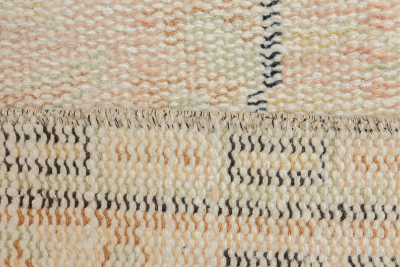 May include: Close-up of a woven rug with a cream, beige, and brown color scheme. The rug has a textured surface and a fringe border.