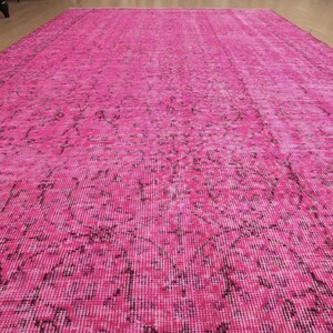 May include: A large, rectangular rug in a vibrant fuchsia colour. The rug features a distressed, vintage-style pattern in darker shades of pink and black. The rug is made of a soft, woven material.