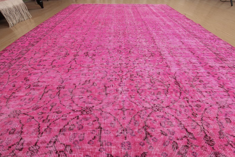 May include: A large, rectangular rug in a vibrant fuchsia colour. The rug features a distressed, vintage-style pattern in darker shades of pink and black. The rug is made of a soft, woven material.