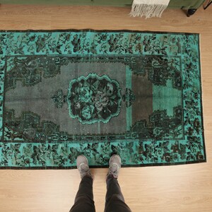 May include: A teal and black vintage rug with a floral pattern. The rug is laid out on a wooden floor.