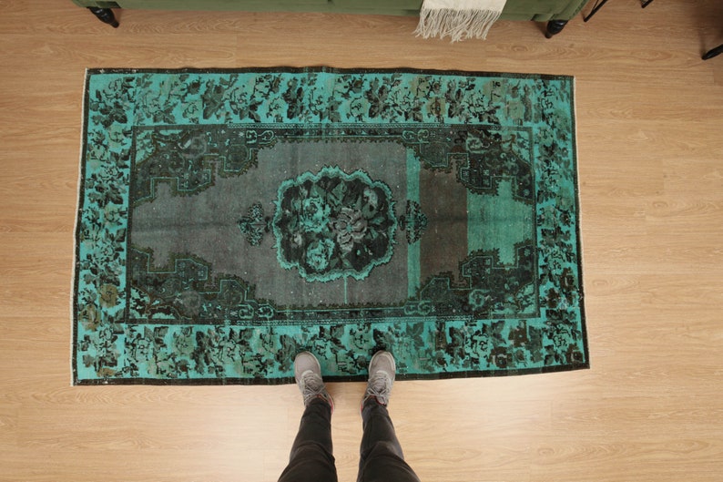 May include: A teal and black vintage rug with a floral pattern. The rug is laid out on a wooden floor.