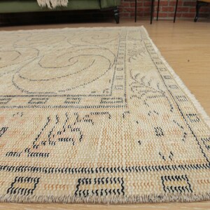 May include: A beige rug with a black and white geometric pattern. The rug has a fringe border.