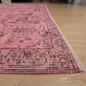 May include: A rectangular area rug featuring a vibrant pink base color with intricate dark brown floral and geometric patterns throughout. The rug has a defined border and short white fringe along the edge, showcasing a woven texture.
