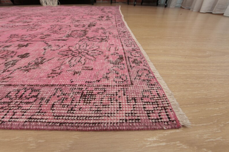 May include: A rectangular area rug featuring a vibrant pink base color with intricate dark brown floral and geometric patterns throughout. The rug has a defined border and short white fringe along the edge, showcasing a woven texture.