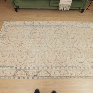 May include: A beige area rug with a geometric pattern of swirling lines. The rug has a dark blue border with a smaller pattern of stylized leaves.