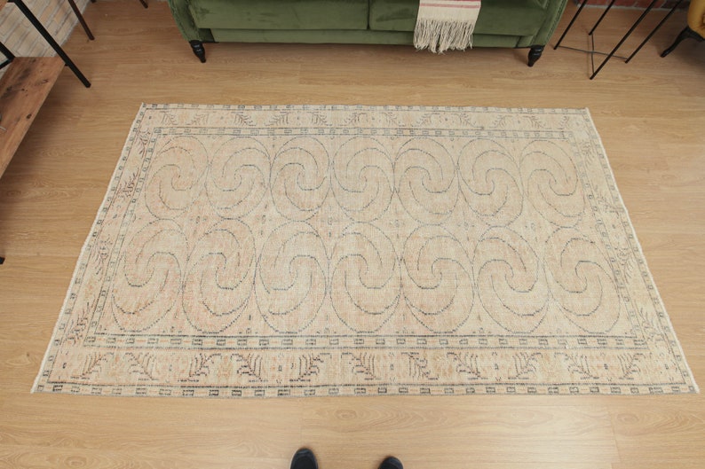 May include: A beige area rug with a geometric pattern of swirling lines. The rug has a dark blue border with a smaller pattern of stylized leaves.