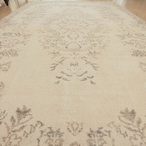 May include: A beige rug with a floral pattern in a darker shade of beige. The rug has a subtle texture and a slightly distressed look.