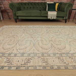 May include: A beige area rug with a swirling pattern in a darker beige color. The rug has a border with a repeating geometric design.