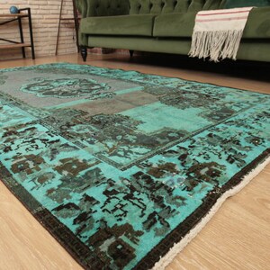 May include: A vintage teal and brown patterned rug with a faded look. The rug has a fringed edge and is laid out on a wooden floor.
