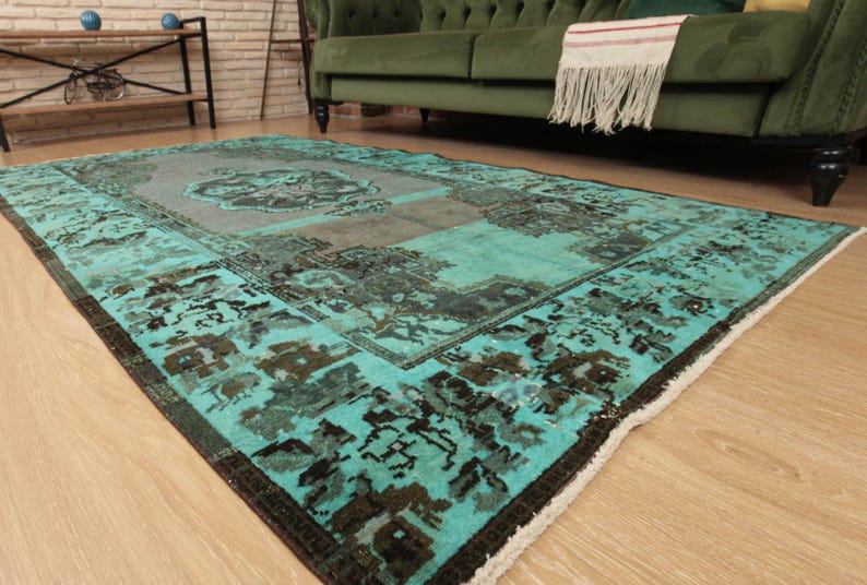 May include: A vintage teal and brown patterned rug with a faded look. The rug has a fringed edge and is laid out on a wooden floor.